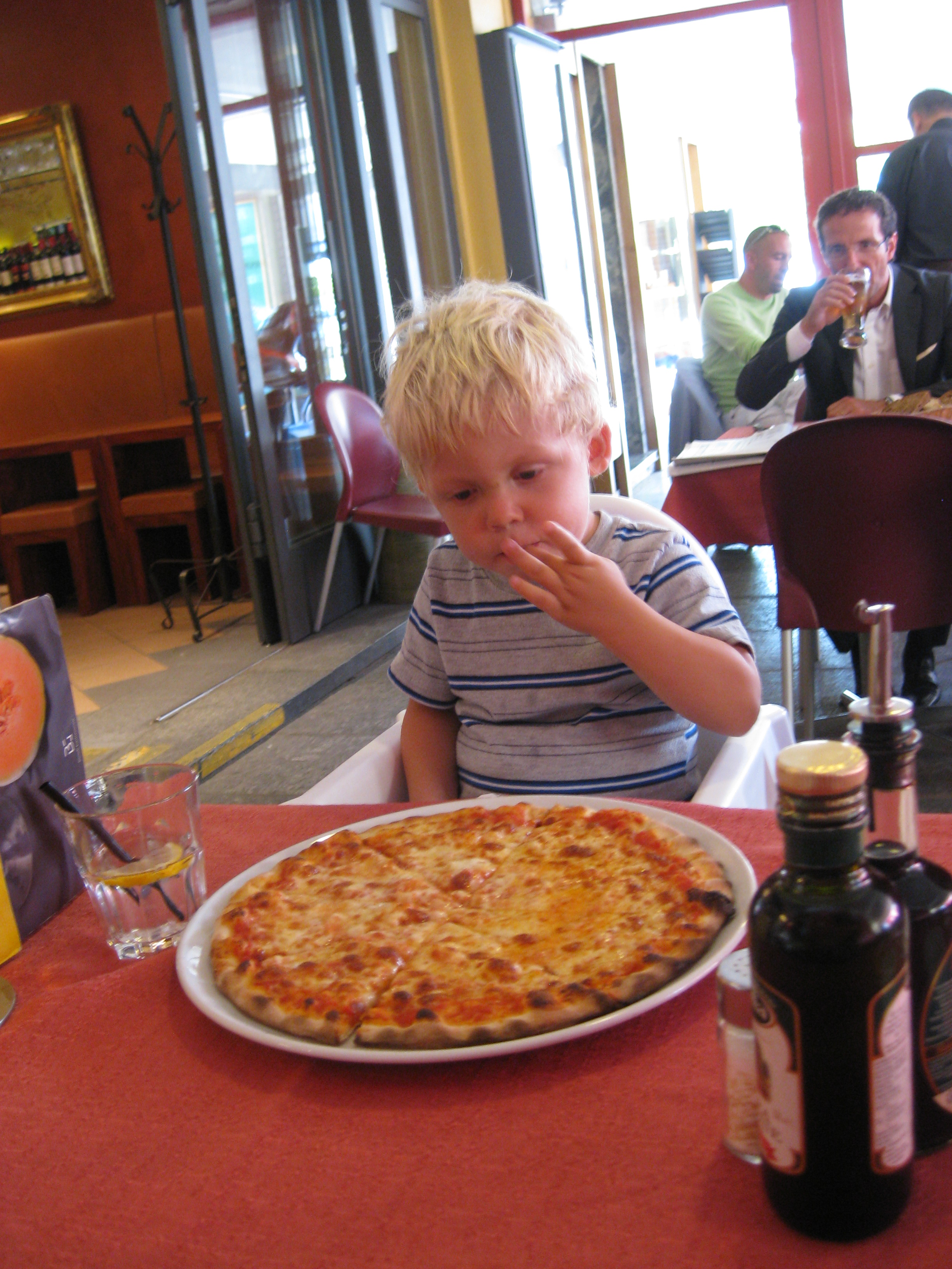 Small child overwhelmed by a large pizza in a restaurant in Switzerland.