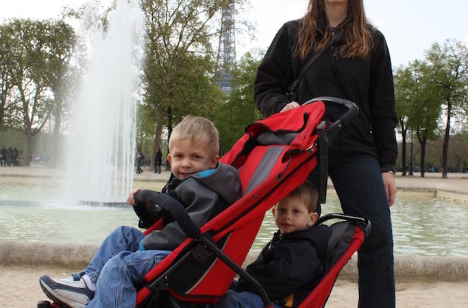 Mom with boys in a stroller in front of a fountain.