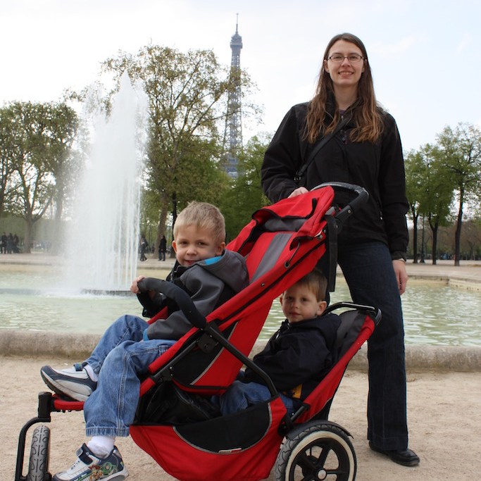 Mom with boys in a stroller in front of a fountain.