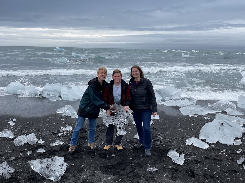 Mom and teenage sons holding giant blocks of ice on Diamond Beach in Iceland.