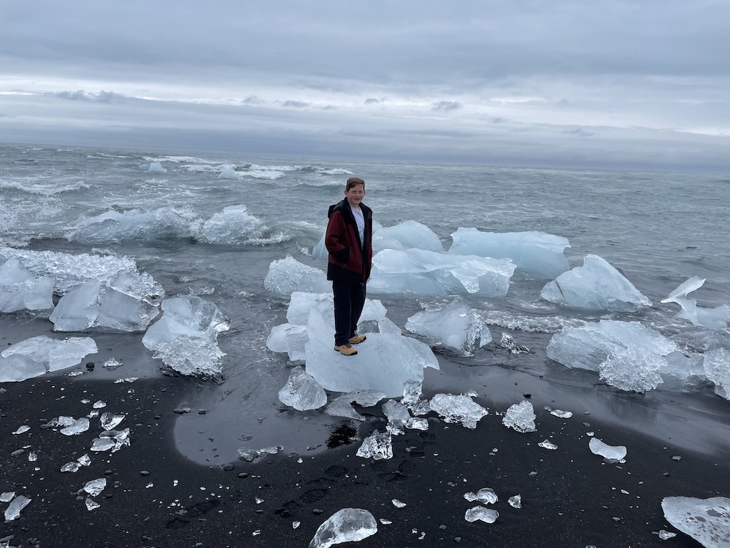 Boy standing on a giant block of ice on Diamond Beach in Iceland.
